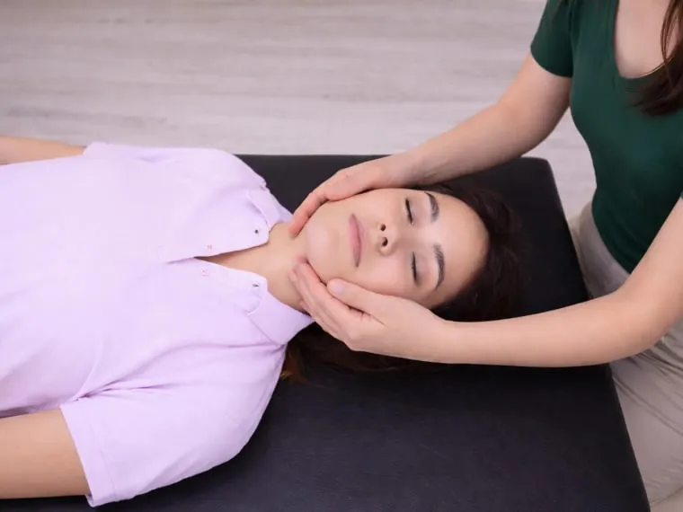A patient lying on a treatment table while a practitioner works on the jaw and neck.